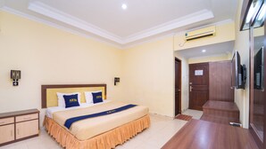 Une chambre d’hôtel comprenant un lit, un bureau en bois, une armoire et un appareil de climatisation.