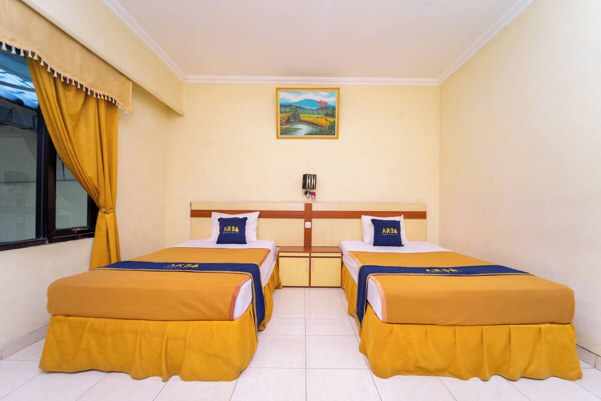 Une chambre d’hôtel avec deux lits simples, un tableau au mur et une fenêtre avec des rideaux.