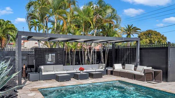 A poolside area with a covered seating area, a pool, and palm trees in the background. - The Blue Heaven/ Poolside Retreat Near Brickell / Sleeps 13 (Miami)