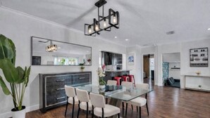 A modern dining area with a glass table and chairs, a dark wooden cabinet, and a large mirror on the wall. - The Blue Heaven/ Poolside Retreat Near Brickell / Sleeps 13 (Miami)