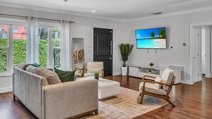 A spacious living room with a large window, a black door, a flat-screen TV, and a cozy seating area. - The Blue Heaven/ Poolside Retreat Near Brickell / Sleeps 13 (Miami)