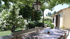 An outdoor patio with a stone wall, a wooden bench, and a table with chairs. - La Maison des Restanques (Cabrières-d'Avignon)