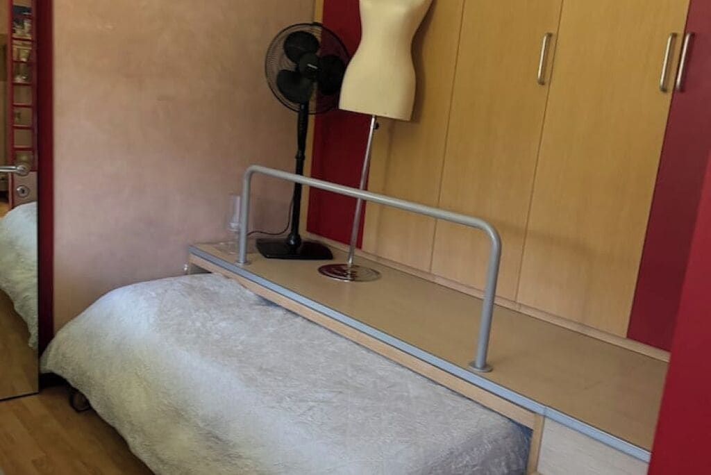 Una camera da letto con un letto, un armadio, una ventola e una lampada.