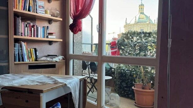 Ein Zimmer mit großem Fenster, Bücherregal, kleinem Tisch und Bett.
