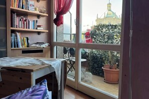 Une pièce avec une grande fenêtre, une bibliothèque, une petite table et un lit.