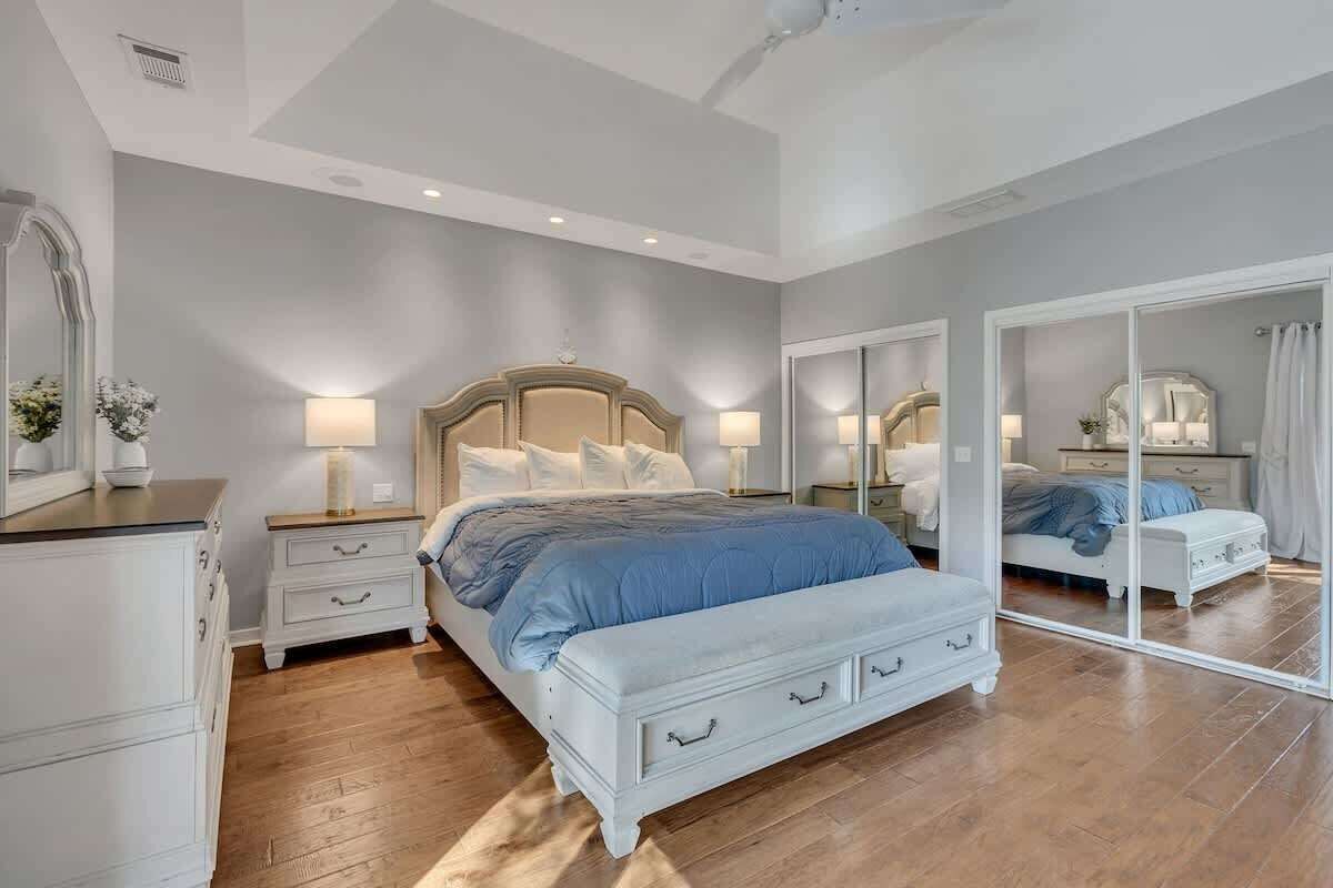 Une chambre à coucher comprenant un lit, des tables de chevet, une commode et un grand miroir.