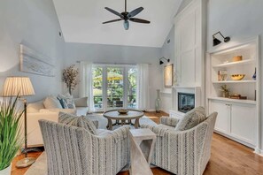 A living room with a white sofa, two armchairs, a coffee table, a ceiling fan, a fireplace, and a bookshelf. - Private Pool, Lagoon View, & Walk to Beach! (Hilton Head Island)