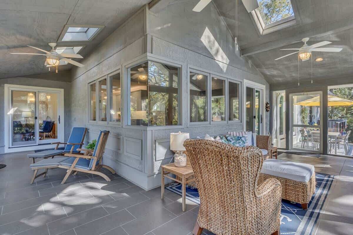 A spacious indoor area with ceiling fans, large windows, and wicker furniture.