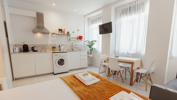 A modern kitchen with a washing machine, a dining area with a table and chairs, and a TV mounted on the wall. - Downtown Formosa Studio by Vacationy (Porto)