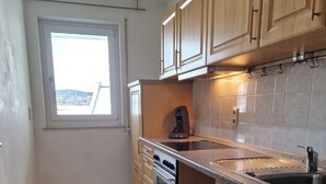 A kitchen with wooden cabinets, a built-in oven, a coffee maker, and a window with a view. - Furnished apartment near Plauen's old market square with sunny balcony (Plauen)