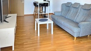 A modern living room with a grey sofa, a white coffee table, a TV on a stand, a dining table with chairs, and a ceiling light. - Furnished apartment near Plauen's old market square with sunny balcony (Plauen)
