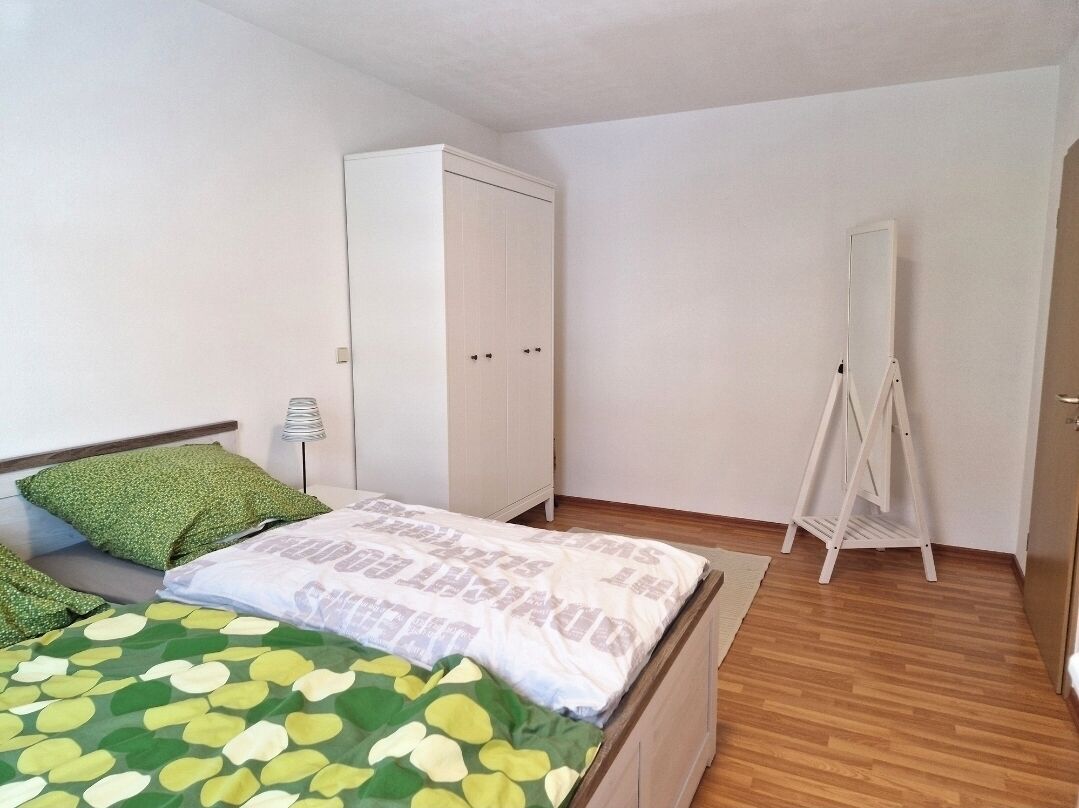 A bedroom with a bed, a wardrobe, a mirror, and a standing lamp.