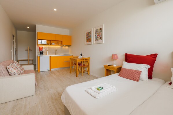 A hotel room with a bed, a small desk, a chair, a sofa, and a kitchenette. - Colorful Studio 1 Municipal Pool by Vacationy (Porto)
