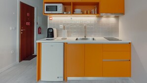 A compact kitchen with orange cabinets, a microwave, a coffee maker, and a dishwasher. - Colorful Studio 1 Municipal Pool by Vacationy (Porto)