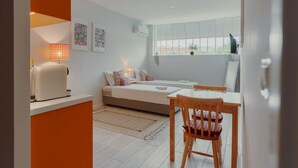 A compact room with a bed, a small table, and a chair. There is a window with blinds, a lamp, and a few wall decorations. - Colorful Studio 1 Municipal Pool by Vacationy (Porto)