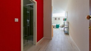 A hallway with a red wall, a glass door leading to a room, and a staircase with a metal railing. - Colorful Studio 1 Municipal Pool by Vacationy (Porto)