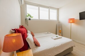 A hotel room with two beds, a window with a plant, a red lamp, and a TV on the wall. - Colorful Studio 1 Municipal Pool by Vacationy (Porto)