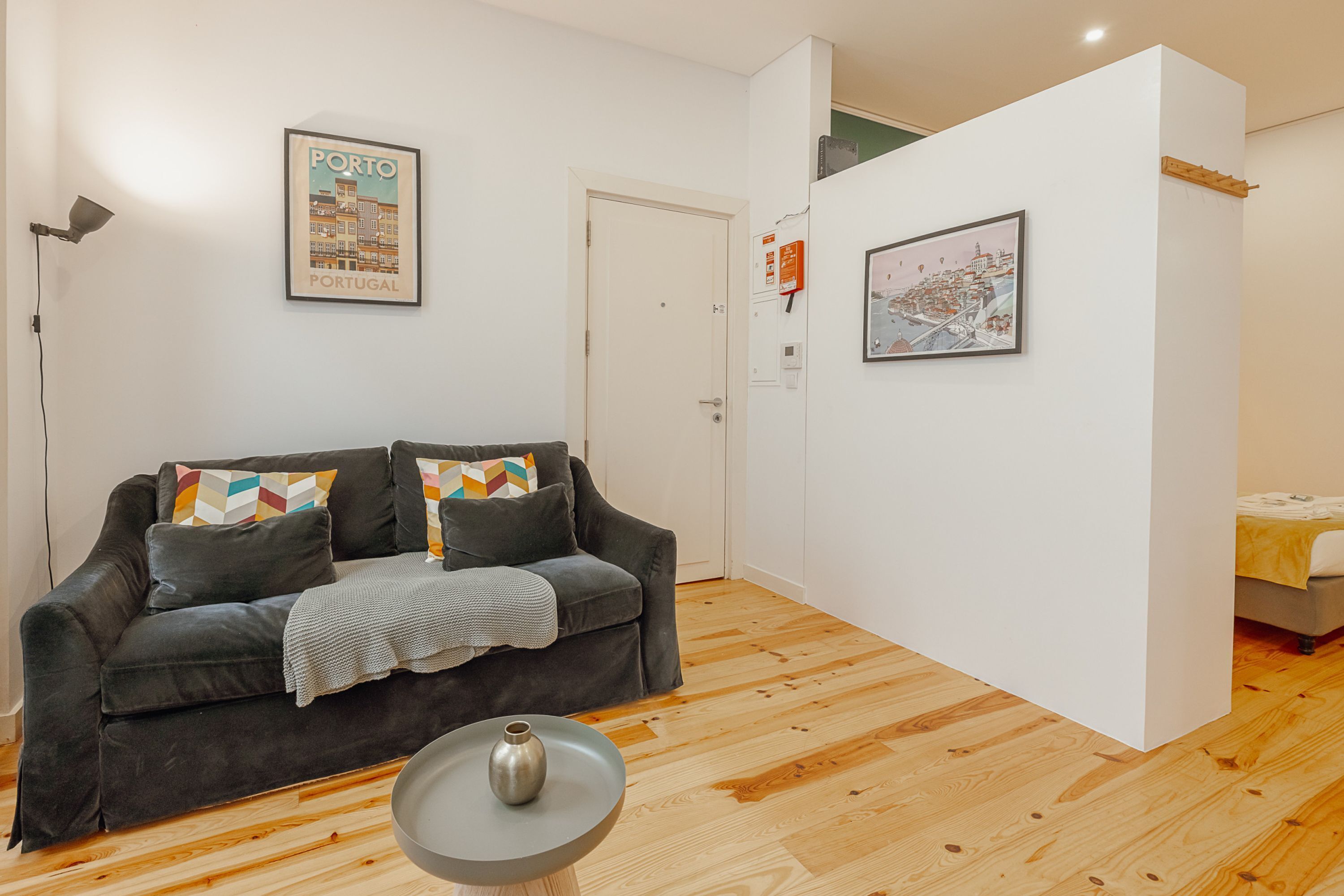 Uma sala de estar moderna com um sofá cinza escuro, uma mesa redonda pequena e duas fotos emolduradas nas paredes.