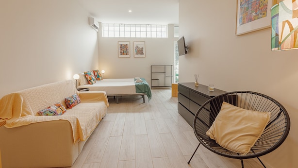 A modern, well-lit room with a sofa, a bed, a black chair, and a TV mounted on the wall. - Colorful Studio 3 Municipal Pool by Vacationy (Porto)
