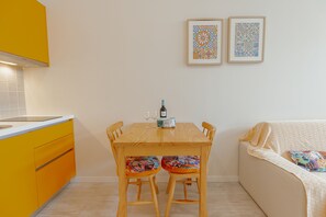 Ένας χώρος τραπεζαρίας με ένα ξύλινο τραπέζι, δύο καρέκλες, έναν καναπέ και μια κουζίνα με κίτρινα ντουλάπια.