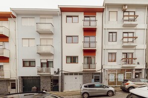 Um edifício residencial com vários andares, varandas, garagem e uma pequena loja no térreo.