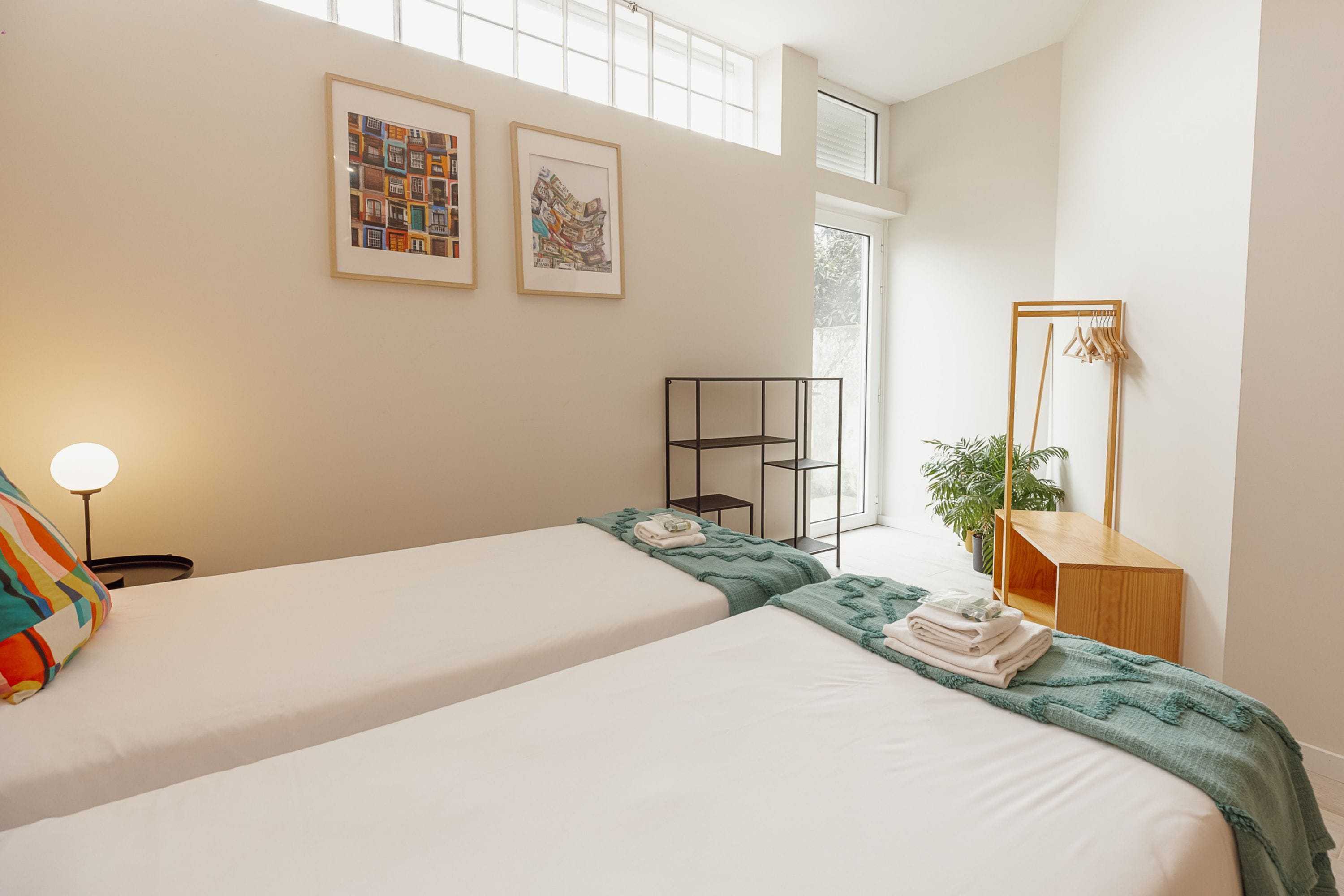 Una camera d'albergo con due letti, un comodino, una lampada, uno specchio e quadri appesi al muro.
