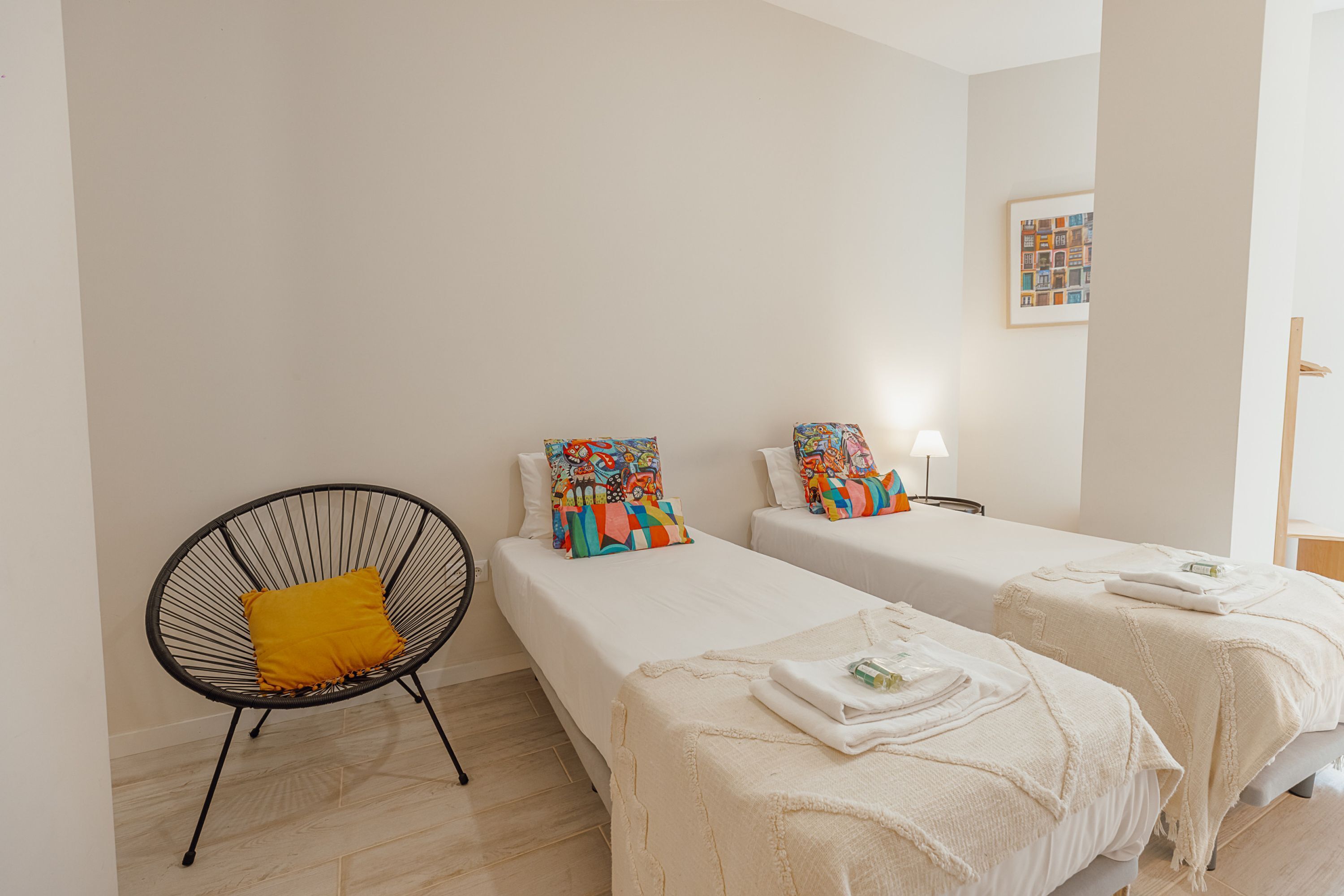 Une chambre d’hôtel avec deux lits, une chaise avec un coussin jaune et un tableau encadré au mur.