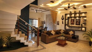 A modern living room with a staircase, a sectional sofa, and a coffee table. - Cascade Villa Spacious 5BHK Luxury Villa (Bengaluru)