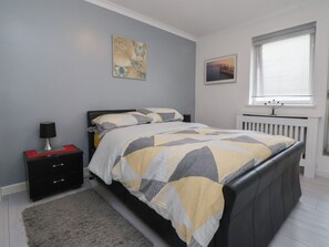 Une chambre à coucher avec un lit, une table de chevet, une lampe et une fenêtre avec des stores.