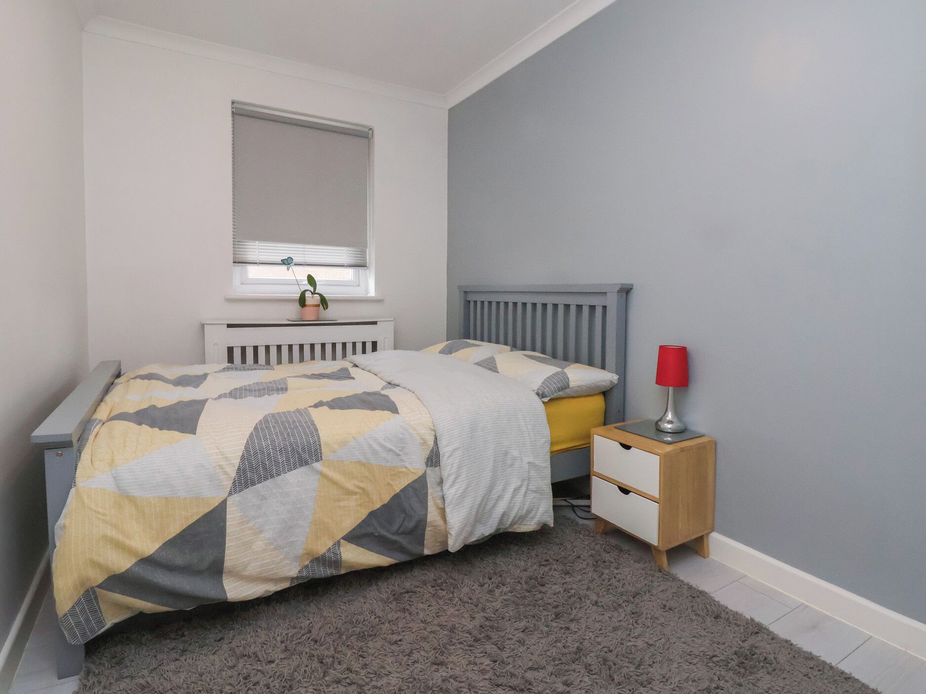 Un dormitorio con cama, mesita de noche, lámpara y ventana con persianas.