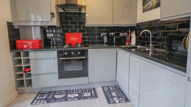 A modern kitchen with white cabinets, black countertops, and a red bread box. - Flat 12 (Wallasey)