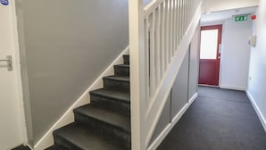 A staircase with white railings and a red door at the top. - Flat 12 (Wallasey)