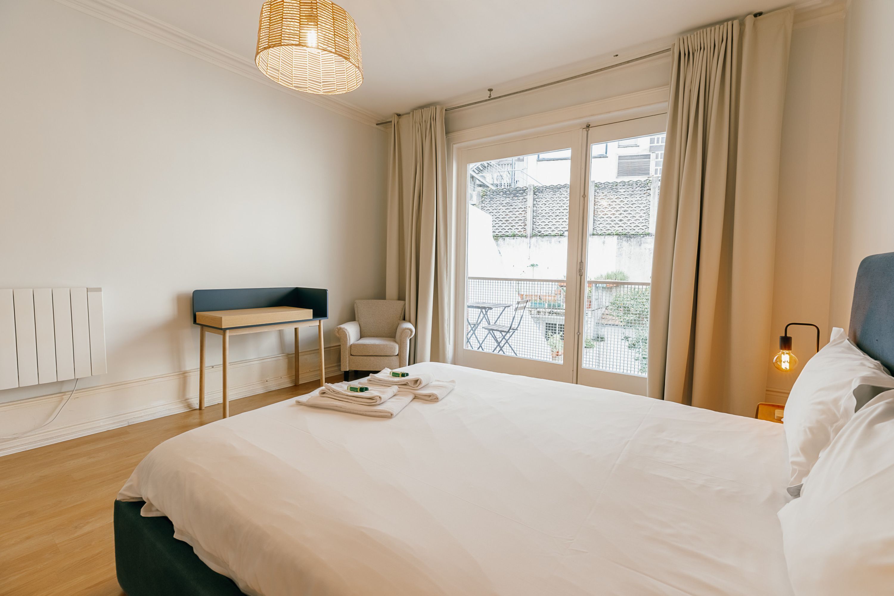 A hotel room with a large bed, a desk, a chair, and a view of the outside.