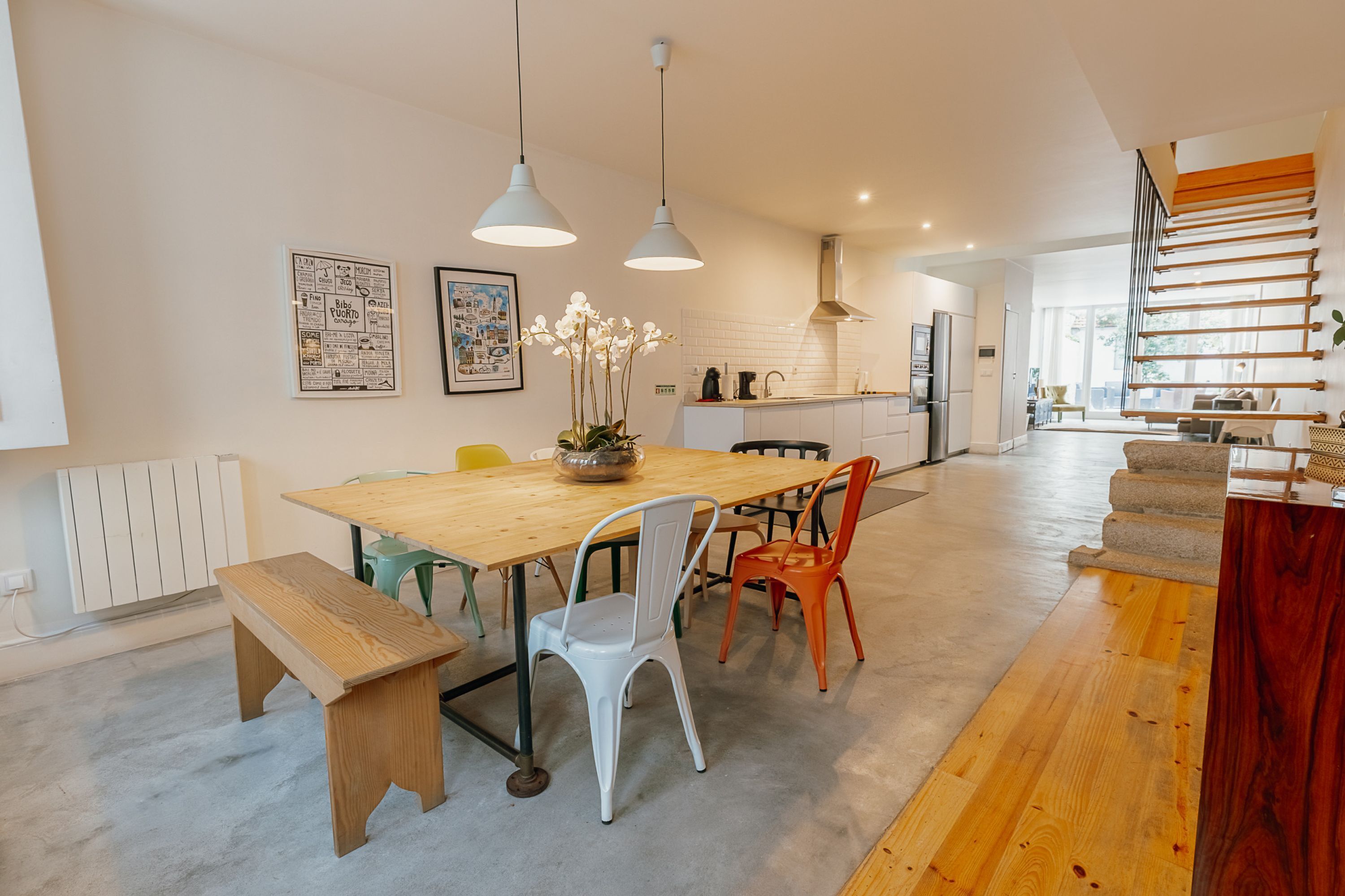 A modern kitchen with a wooden table, white chairs, and hanging pendant lights.
