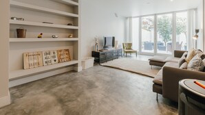Moderni olohuone, jossa on harmaa betonilattia, sohva, televisio ja koriste-esineillä täytetty kirjahylly.