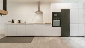 Moderni keittiö, jossa on valkoiset kaapit, ruostumattomasta teräksestä valmistettu liesituuletin, sisäänrakennettu uuni ja musta jääkaappi.