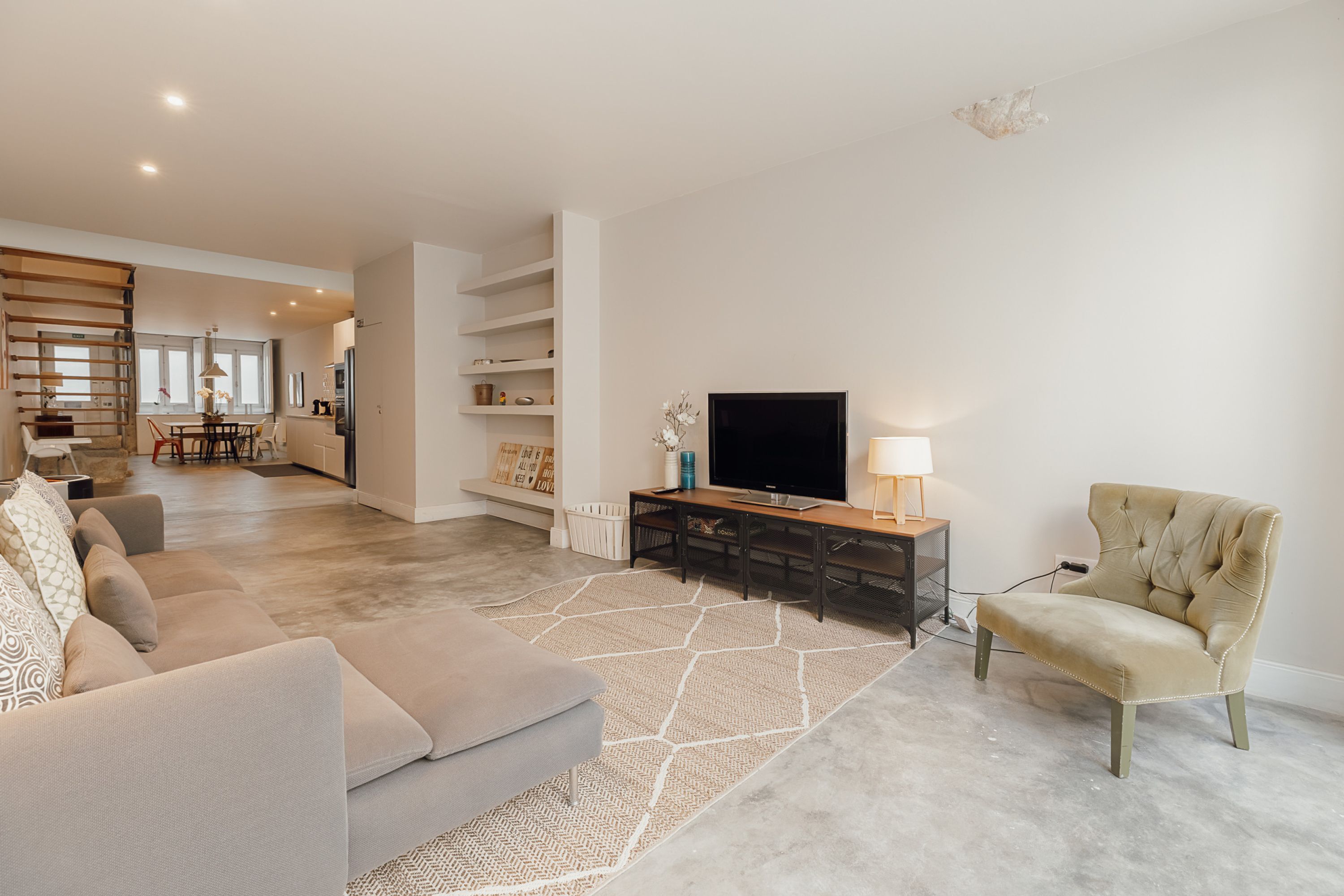 Un salón amplio con un sofá, televisión y lámpara. Se aprecia un comedor al fondo con mesa y sillas.