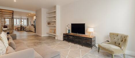 Un salón amplio con un sofá, televisión y lámpara. Se aprecia un comedor al fondo con mesa y sillas.
