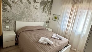 Quarto moderno com cama, mesas de cabeceira, um mural na parede, uma luminária no teto e uma janela com cortinas.