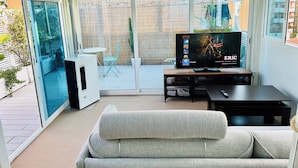 Sala de estar com sofá cinza, TV em um móvel e porta de vidro deslizante para um pátio.