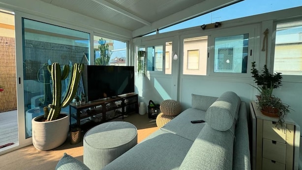 Uma sala de estar moderna com uma televisão de tela grande, um sofá cinza e uma planta cacto.