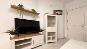 Un salon moderne doté d’un téléviseur à écran plat, d’étagères blanches et de plantes en pot.