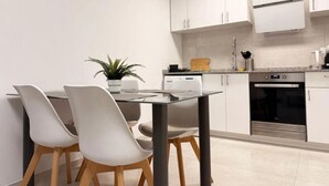 Une cuisine moderne avec des meubles blancs, un four encastré et un coin repas comprenant une table et des chaises en verre.