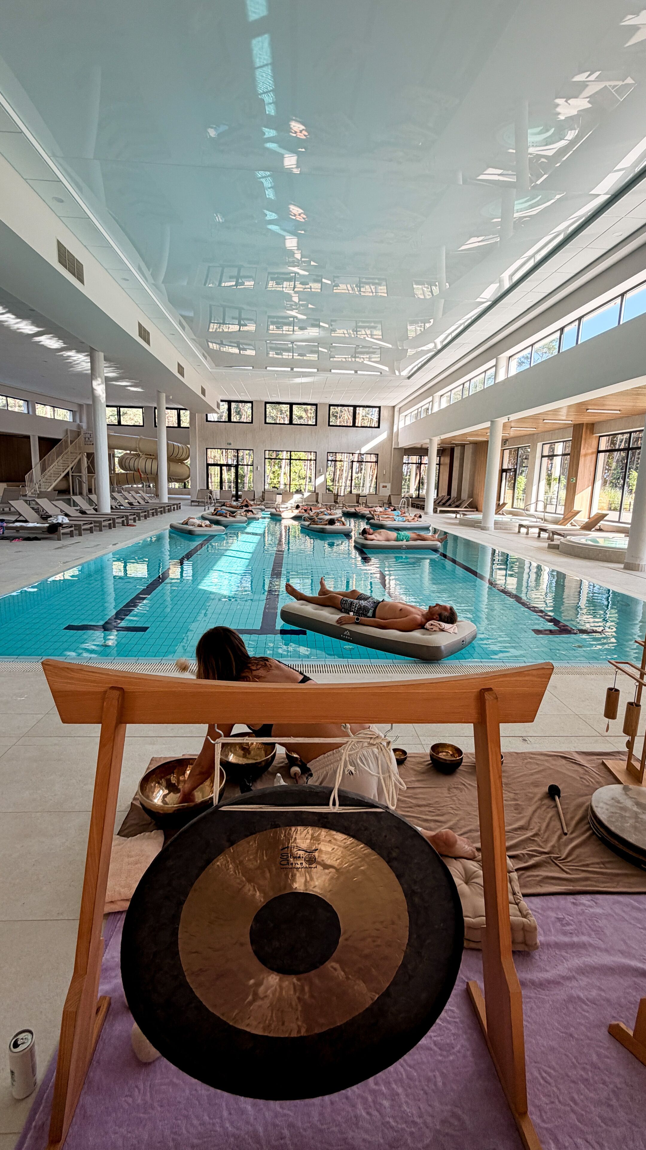 Una piscina interior con varias pistas, tumbonas y un techo con tragaluces.