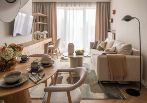Una sala de estar moderna con un sofá, una mesa de centro, una mesa de comedor y sillas. Hay un televisor montado en la pared y una lámpara de pie.