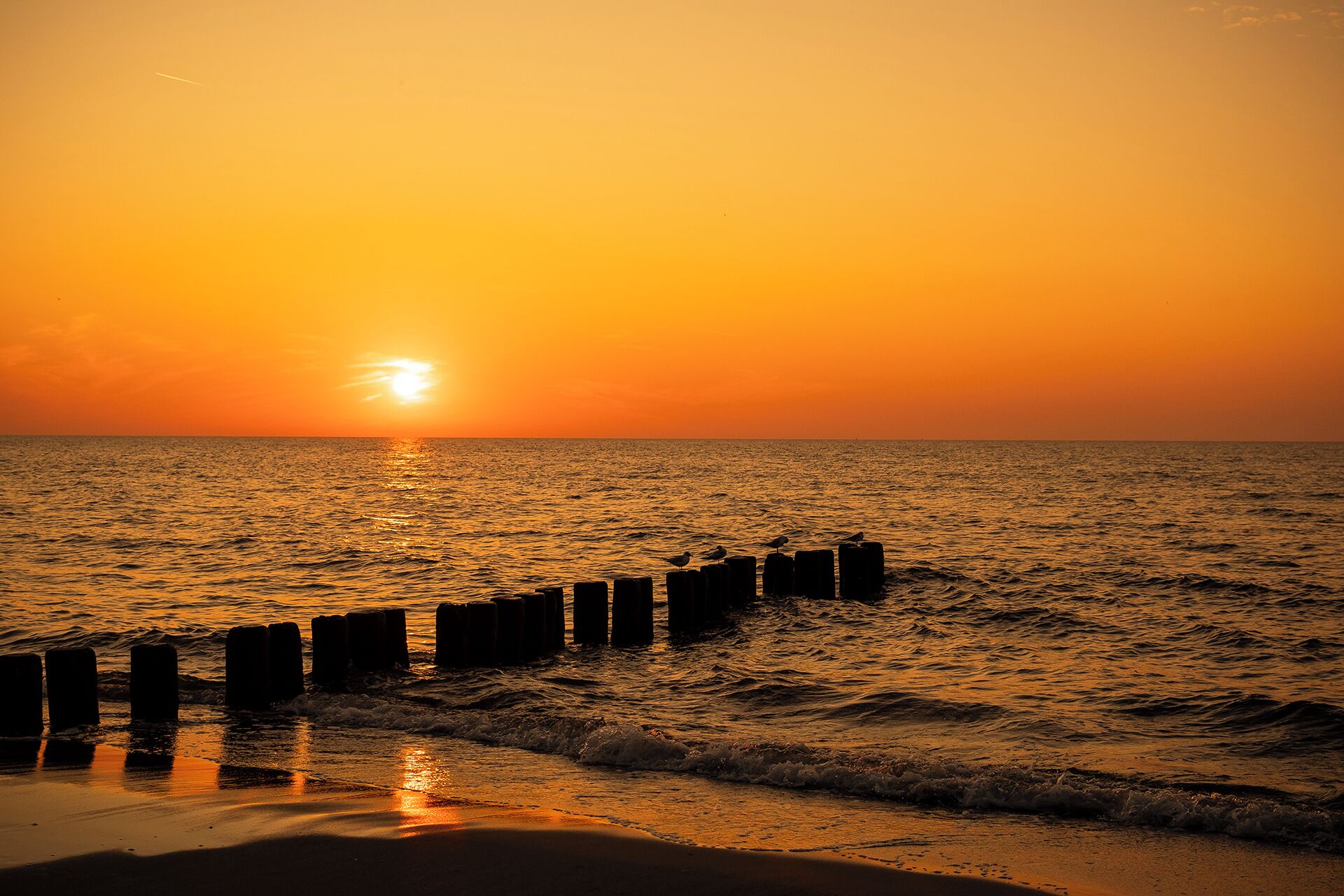 A sunset over the ocean with a wooden pier extending into the water.