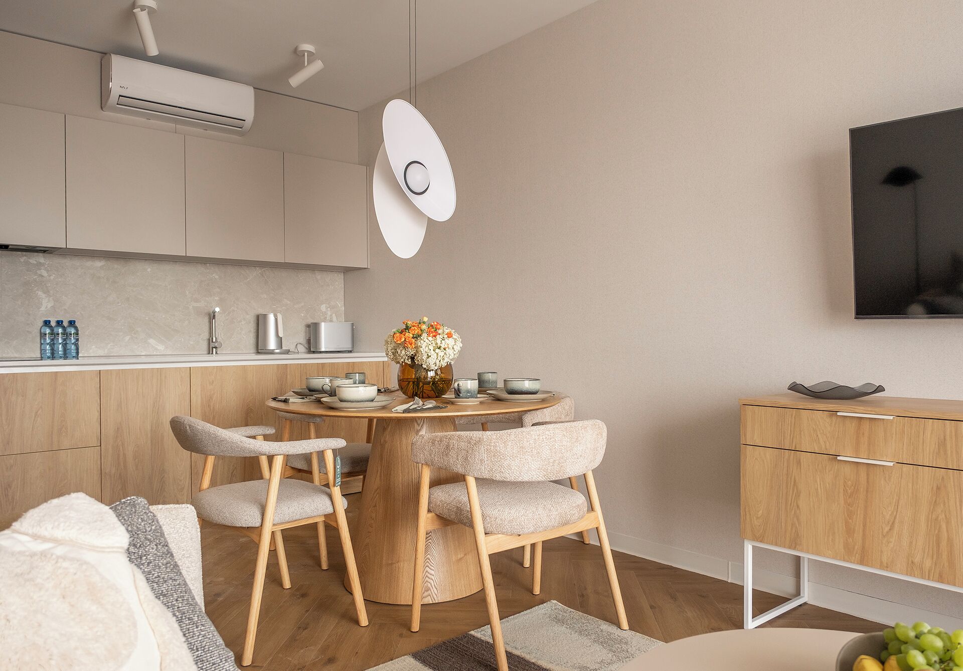 Eine moderne Küche mit einem runden Esstisch, Holzstühlen und einem Blumenstrauß.