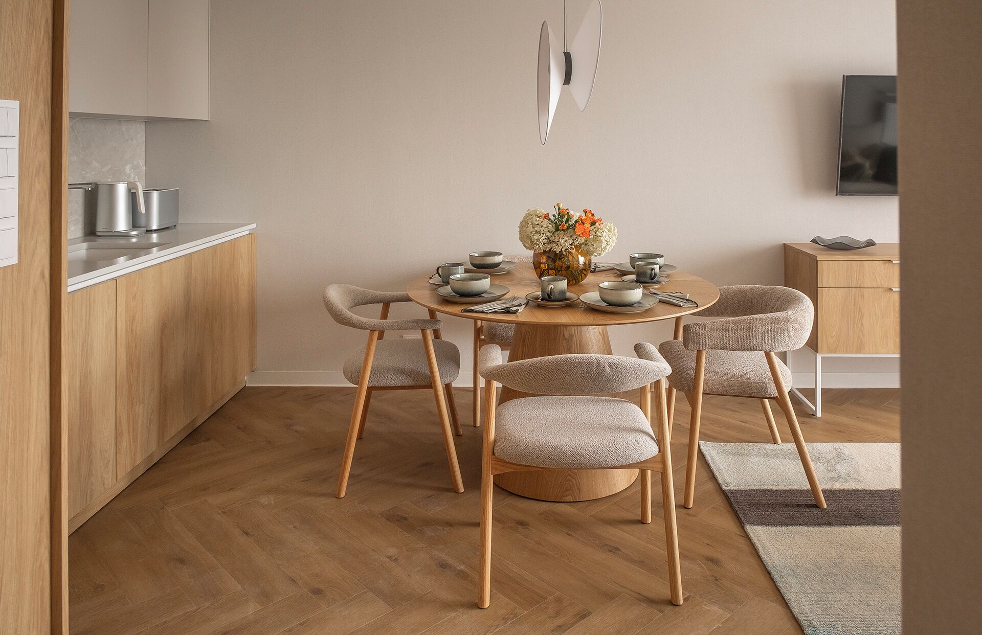 A modern kitchen with wooden cabinets, a round dining table with six chairs, and a vase of flowers.