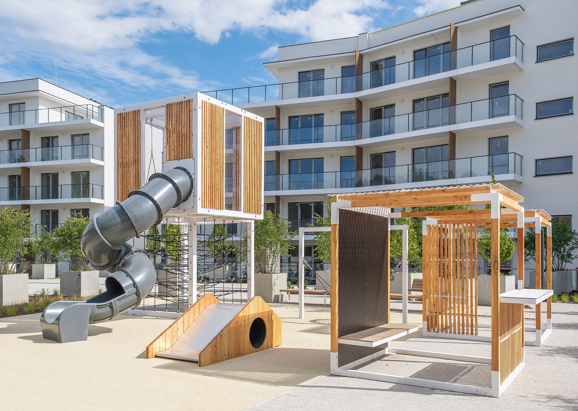 Un terrain de jeux équipé d’un toboggan et de structures d’escalade, entouré d’immeubles d’appartements modernes.