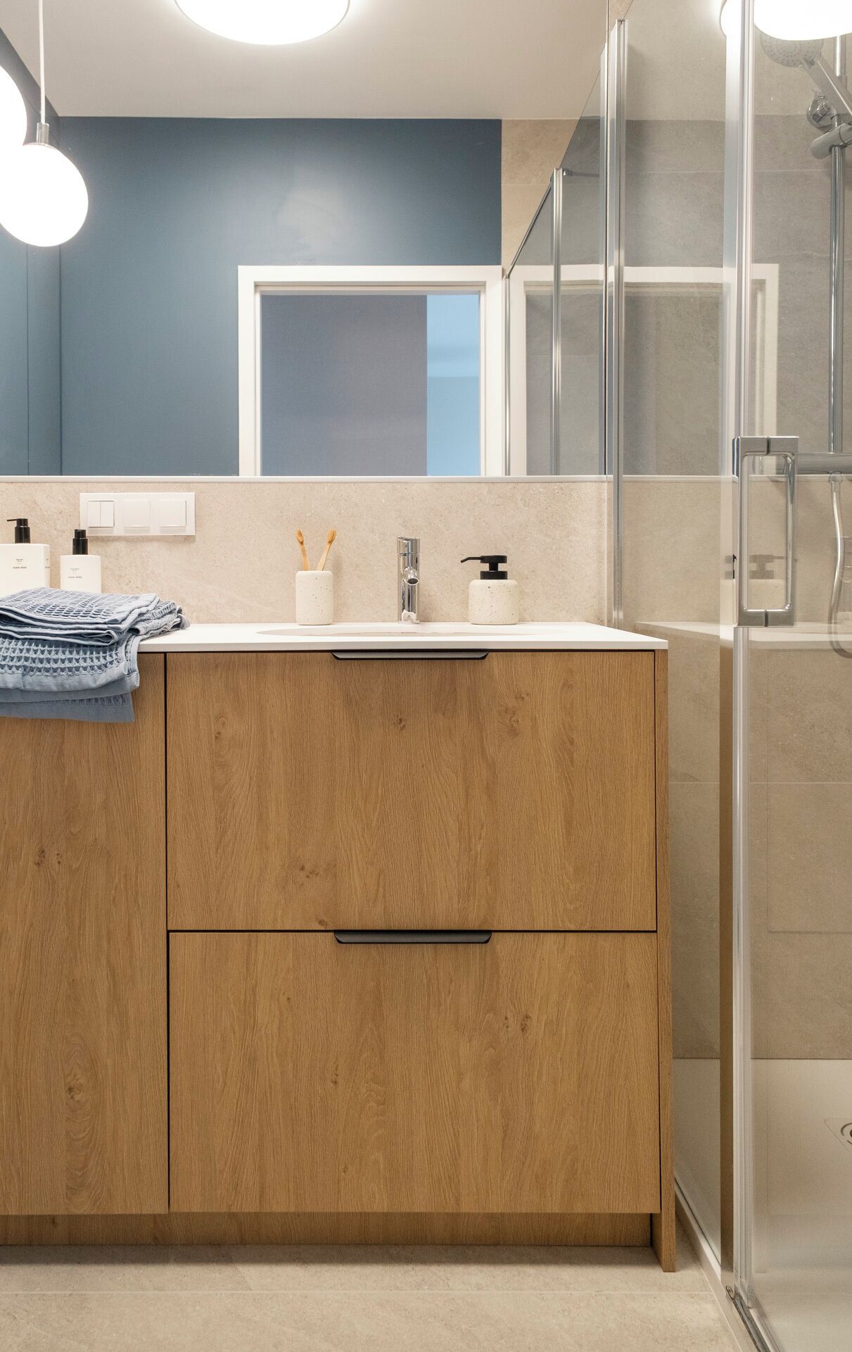 Un baño moderno con tocador de madera, cabina de ducha con mampara de vidrio y pared decorada en tono azul.
